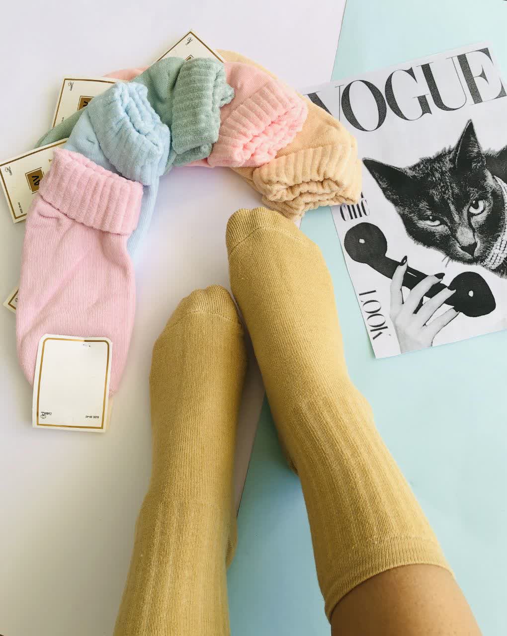 جوراب زنانه لب‌برگرد حوله‌ای در رنگ‌های پاستلی شامل صورتی، آبی، سبز نعنایی، کرم و خردلی، چیده‌شده به‌صورت نیم‌دایره روی زمینه آبی روشن. یک جفت جوراب خردلی در پاها دیده می‌شود. مناسب فصل زمستان، گرم و نرم با طراحی فانتزی.